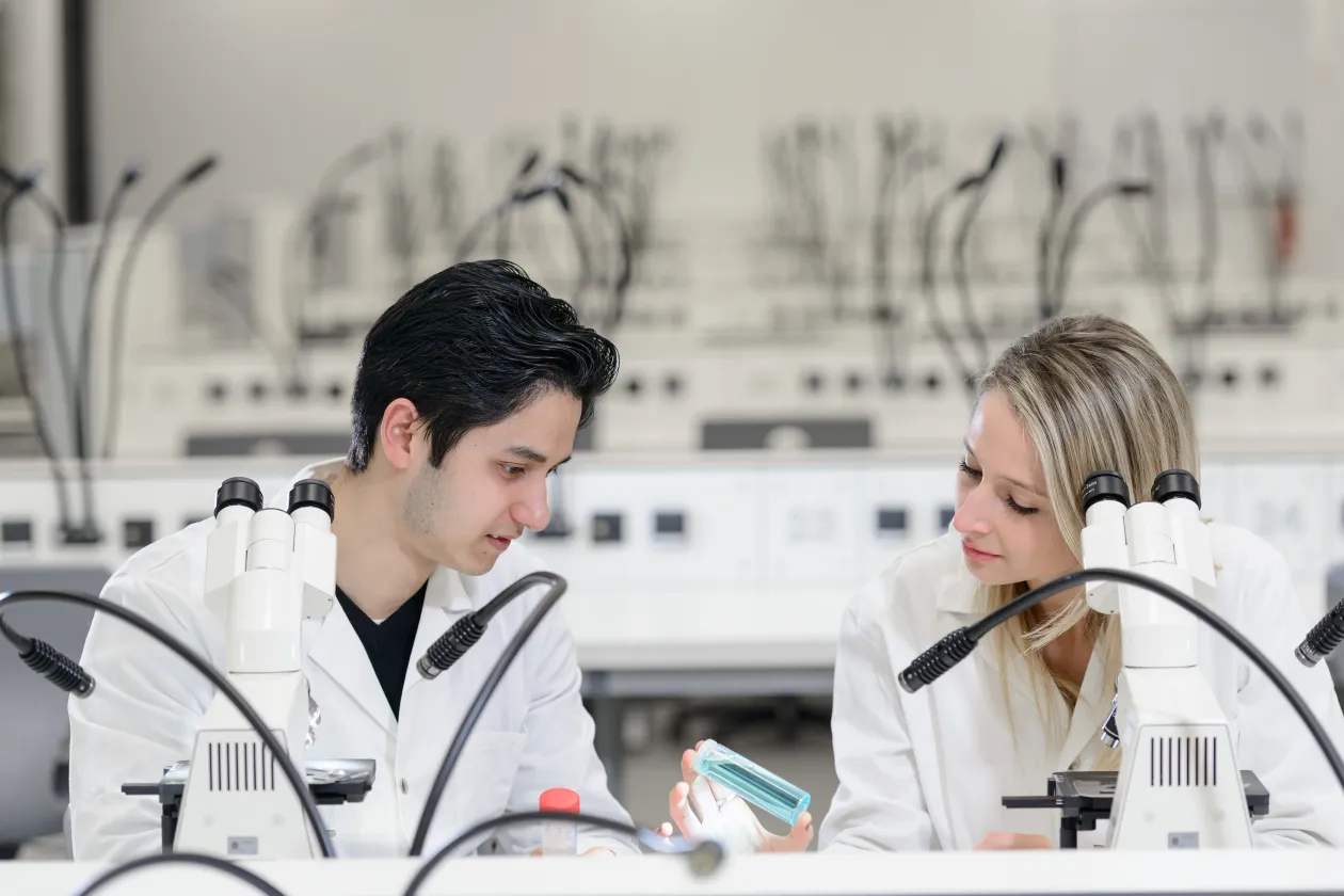 Zwei Schüler in Kitteln vorm Mikroskop